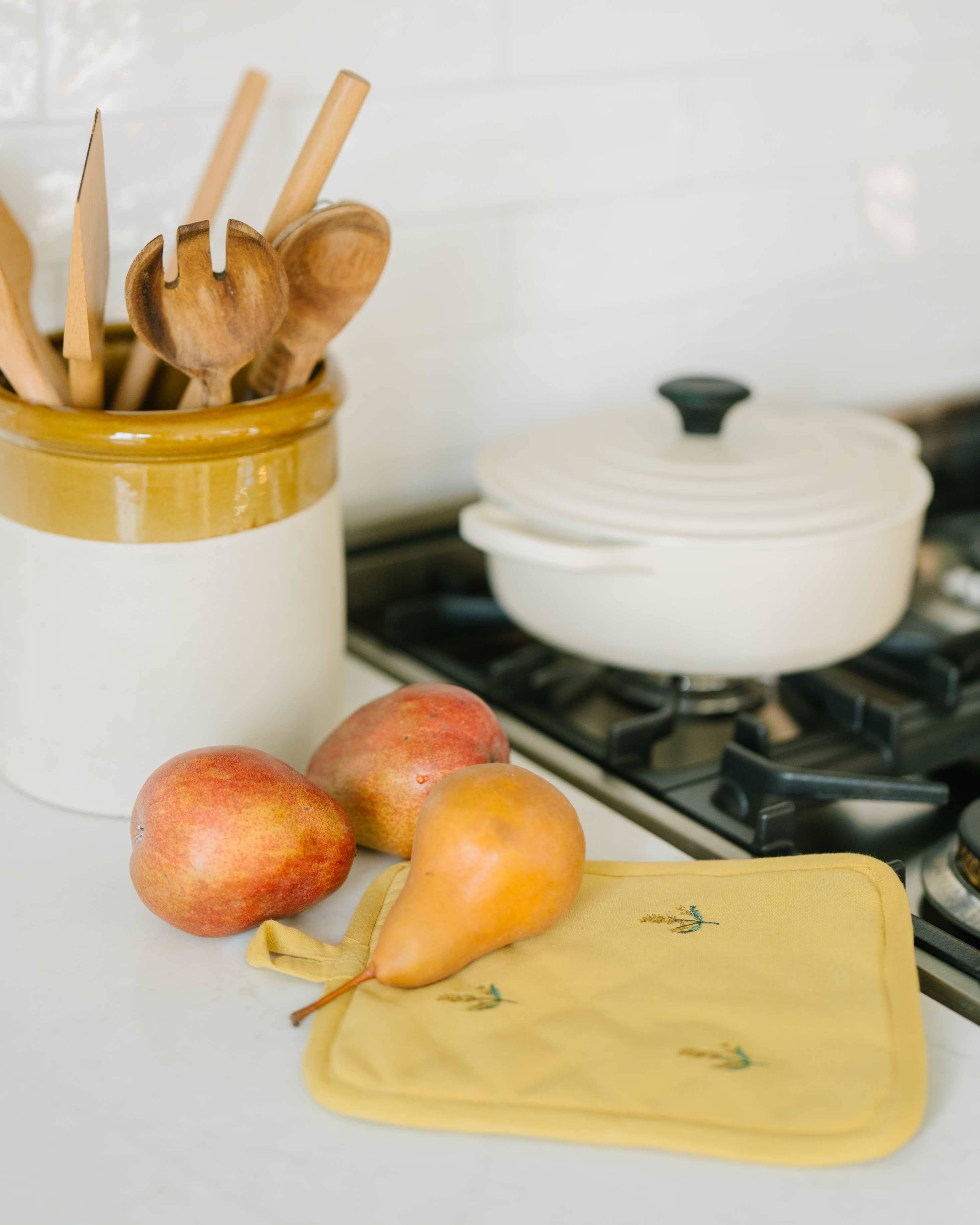 Kitchen counter with apples, pears, and a yellow pot holder next to a white pot on a stove.