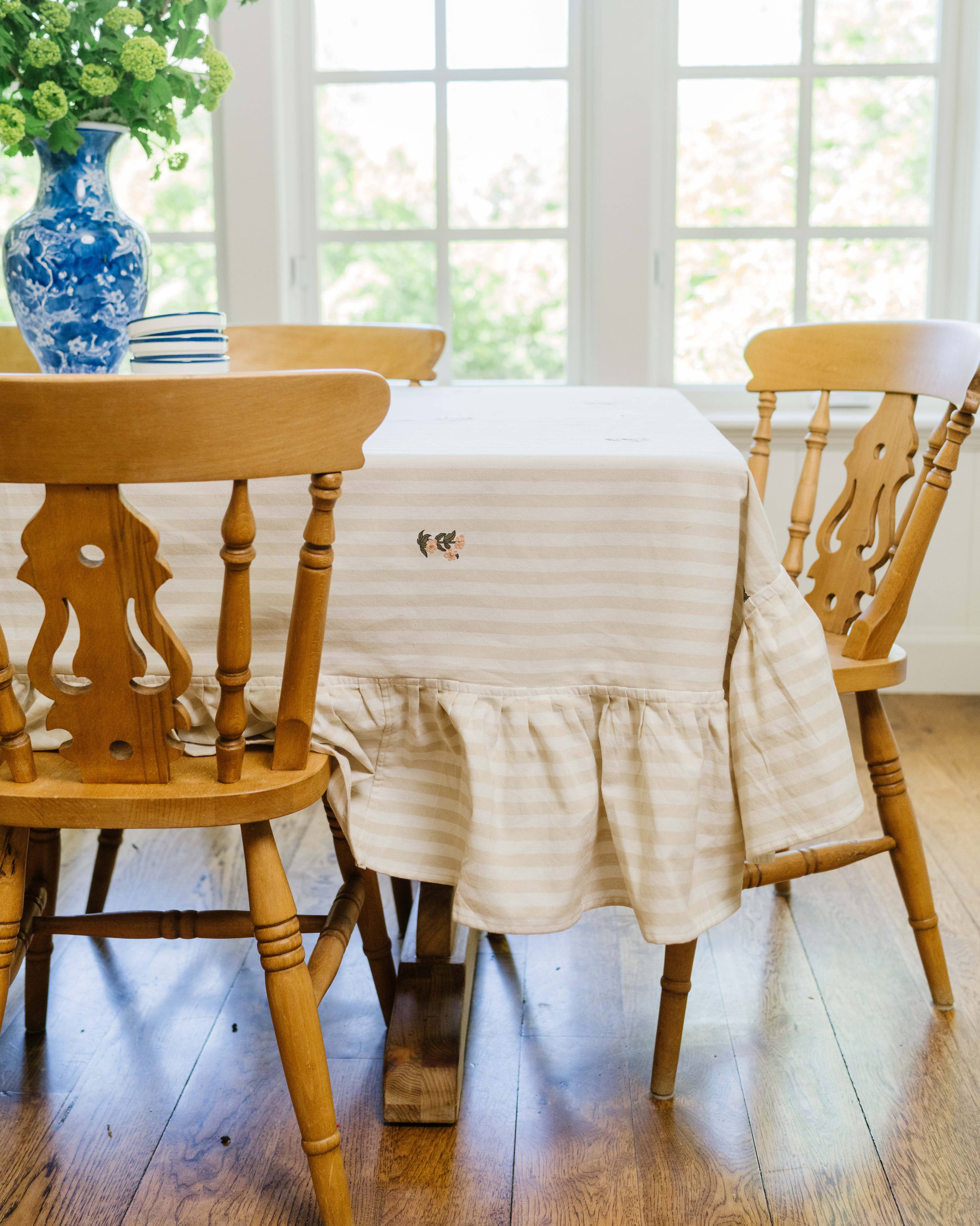 Dining table with a striped tablecloth and wooden chairs in a bright room.