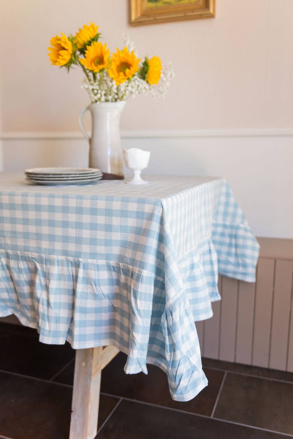 Dining table with a blue gingham tablecloth, yellow flowers in a vase, and plates.