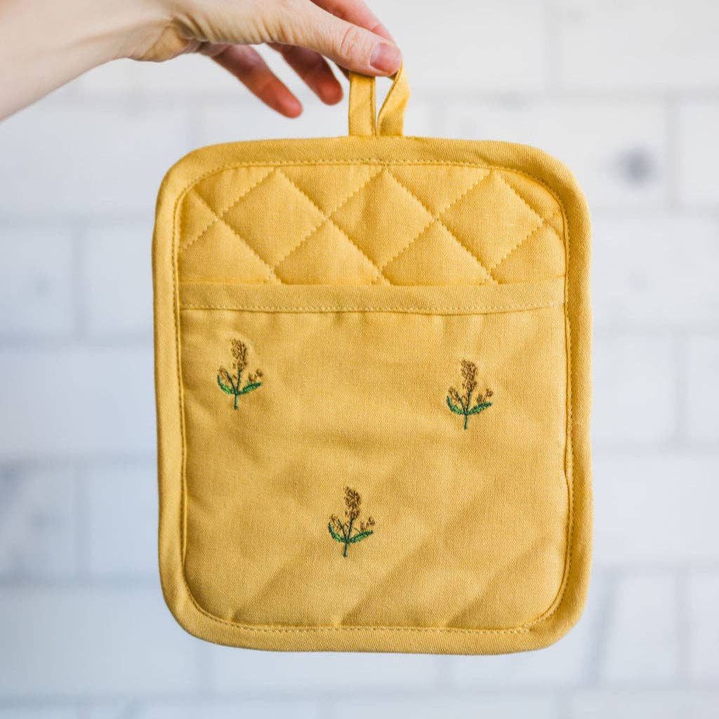 Yellow quilted pot holder with floral embroidery held by a hand on a light background