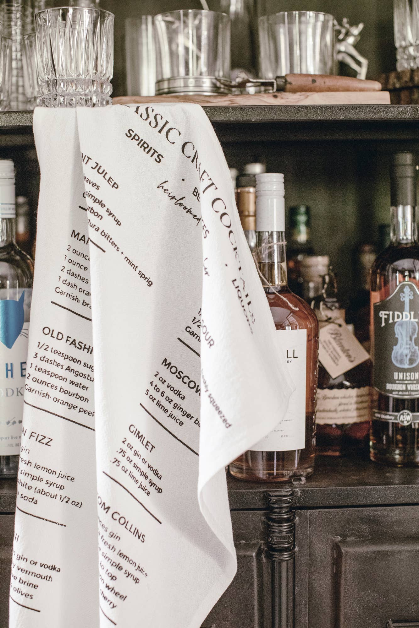 White towel with text draped over a bar setup with bottles and glasses.