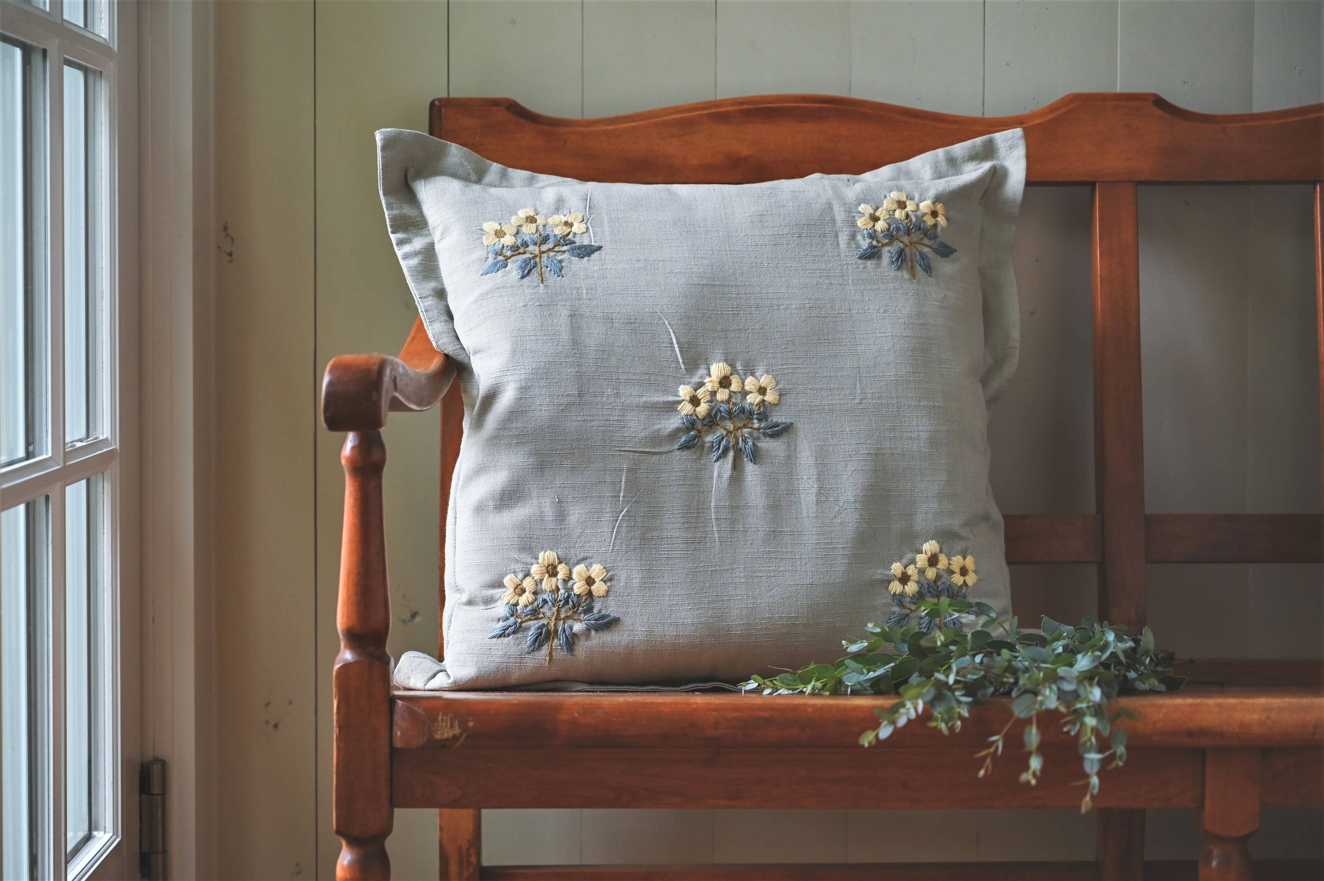 Decorative pillow with floral embroidery on a wooden bench by a window.