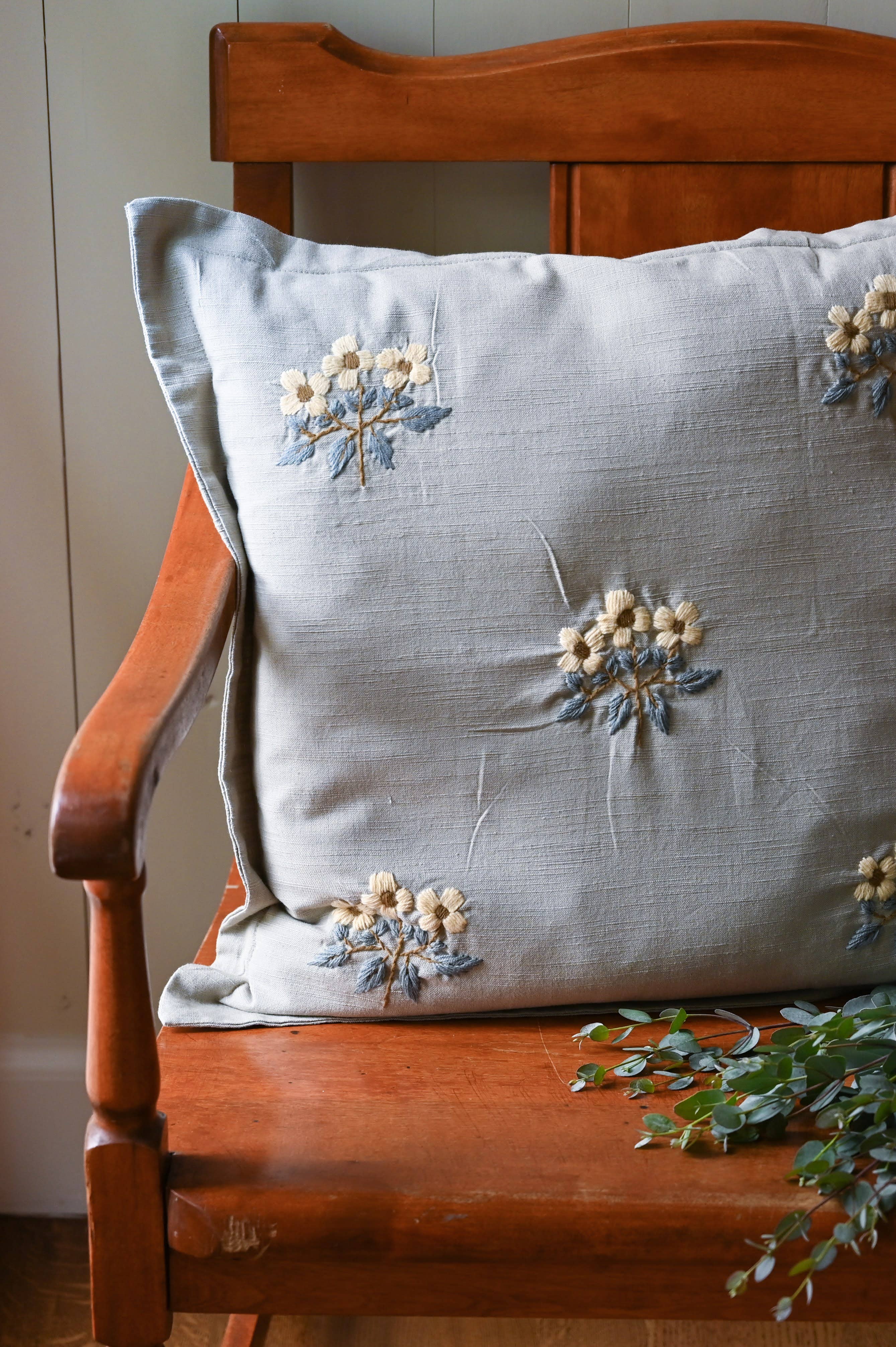 Embroidered floral pillow on a wooden chair with a neutral background