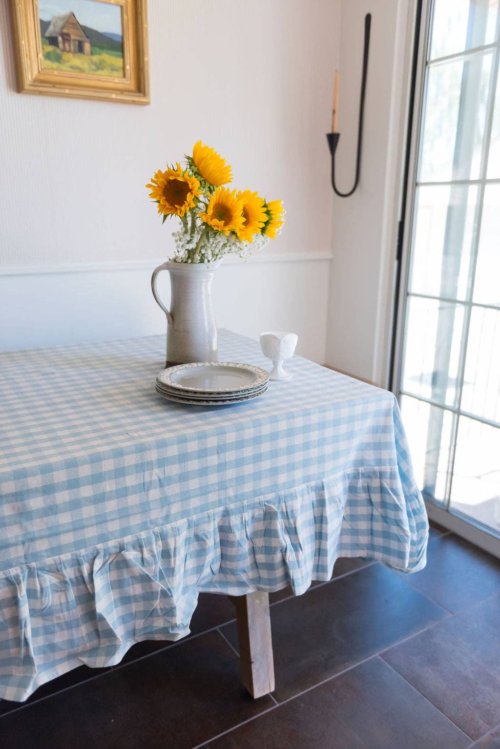 Table with a blue and white gingham tablecloth, sunflowers in a vase, and plates.
