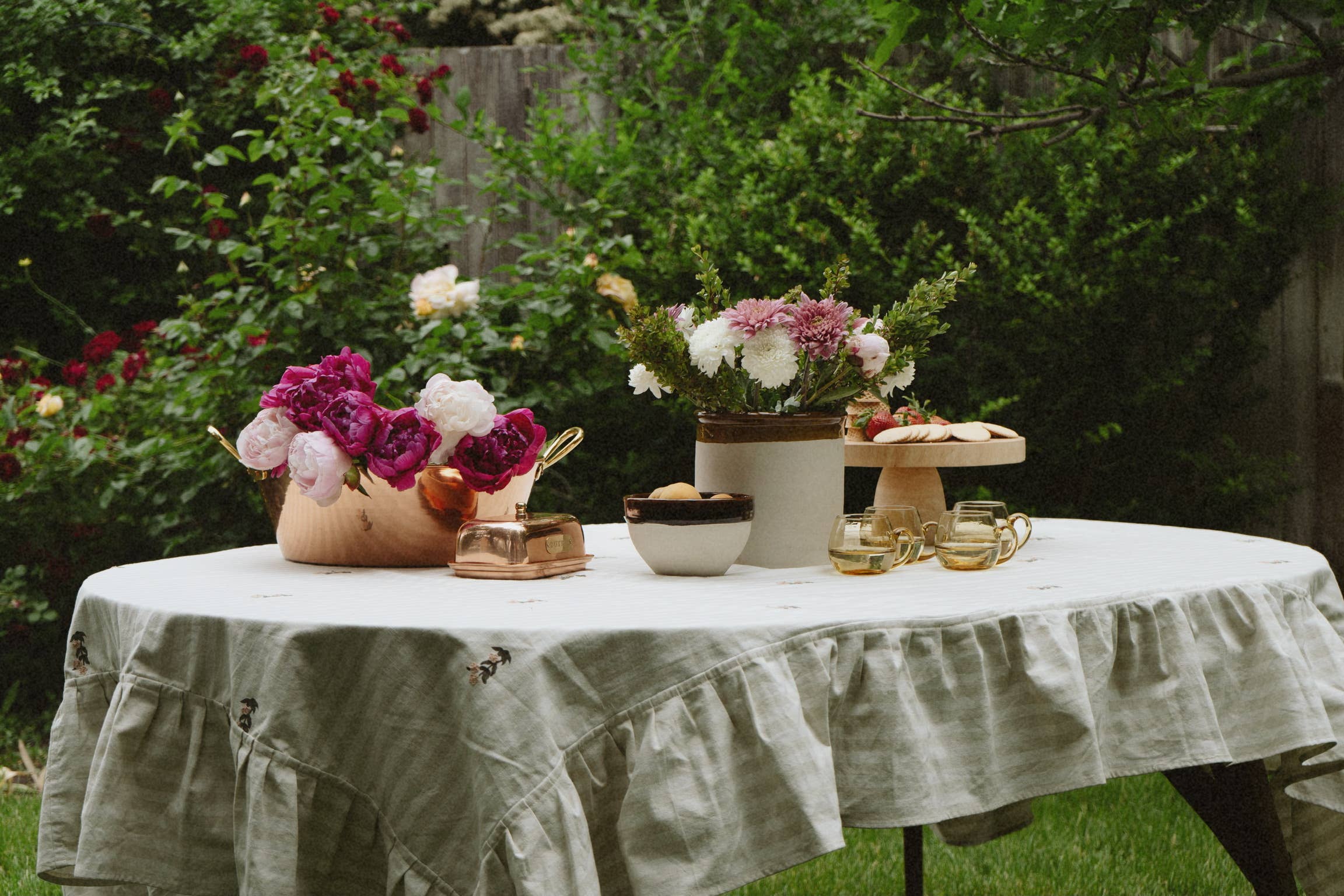 Outdoor table setting with flowers, cake, and tea pots on a white tablecloth.