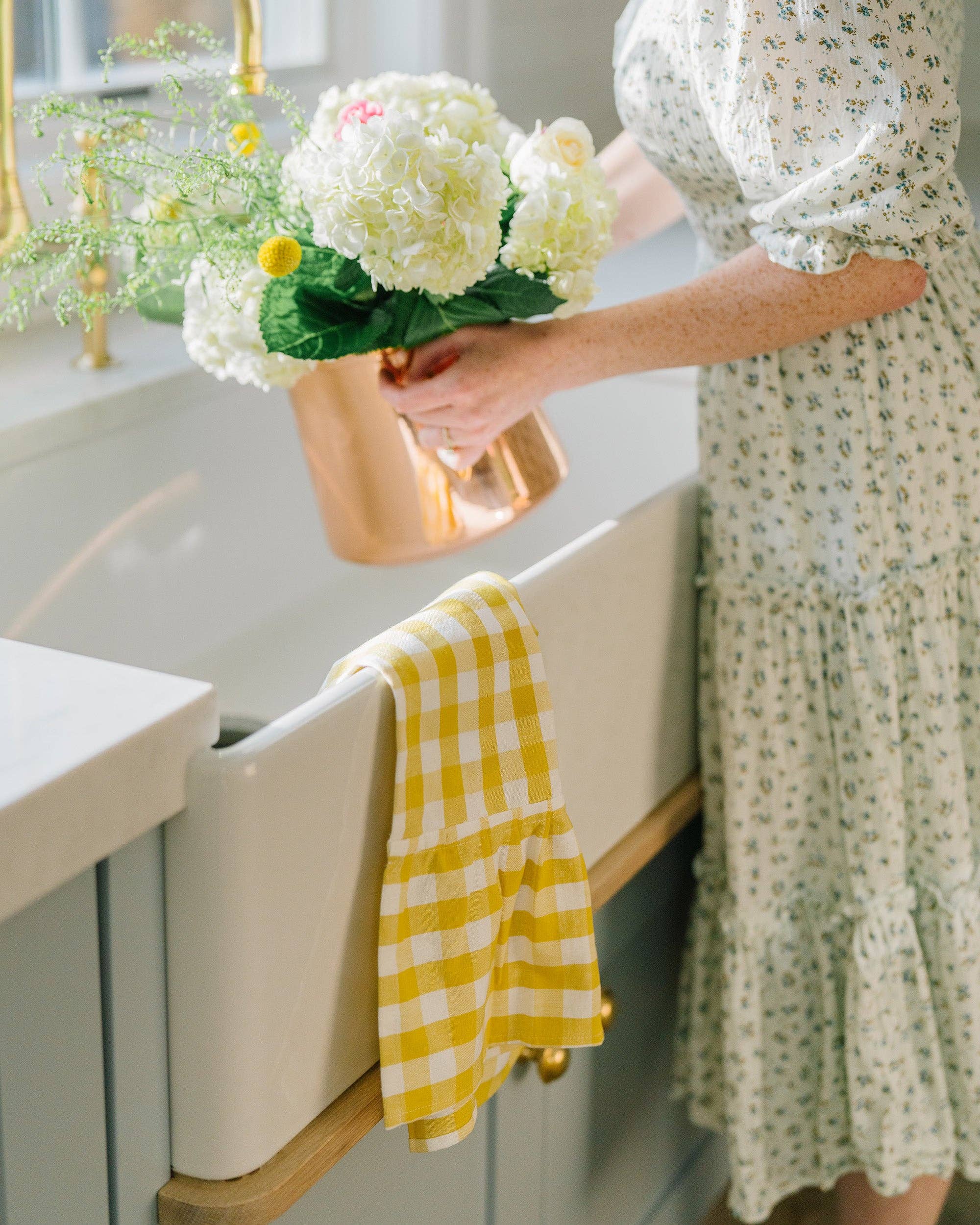 Person holding a bouquet of flowers in a kitchen with a yellow gingham towel on the sink.