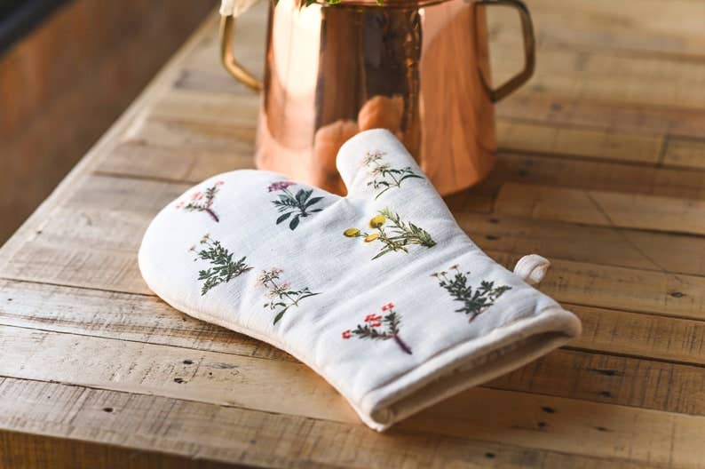 Floral-patterned oven mitt on a wooden surface with a copper pot in the background