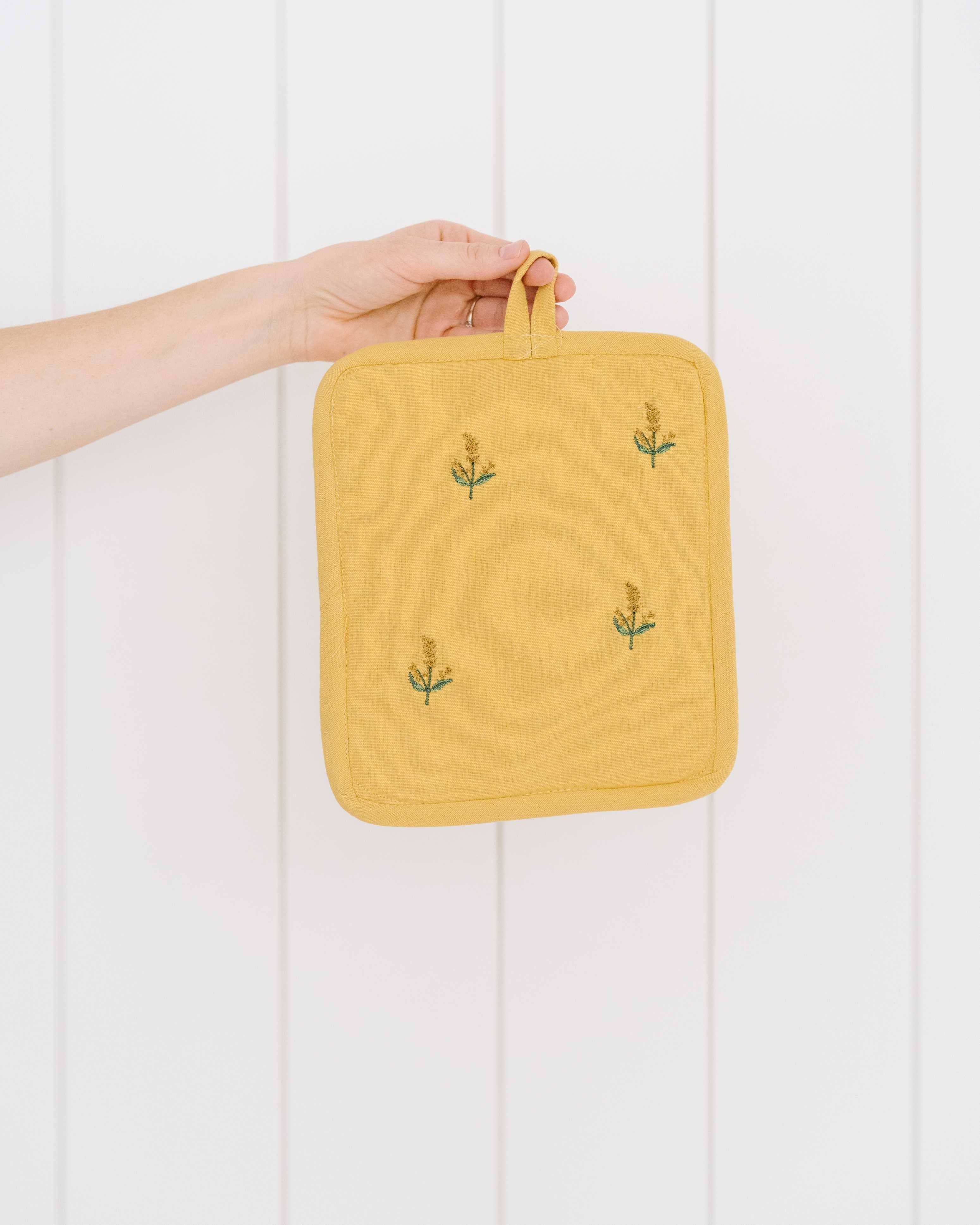 Yellow pot holder with floral patterns held by a hand against a white background