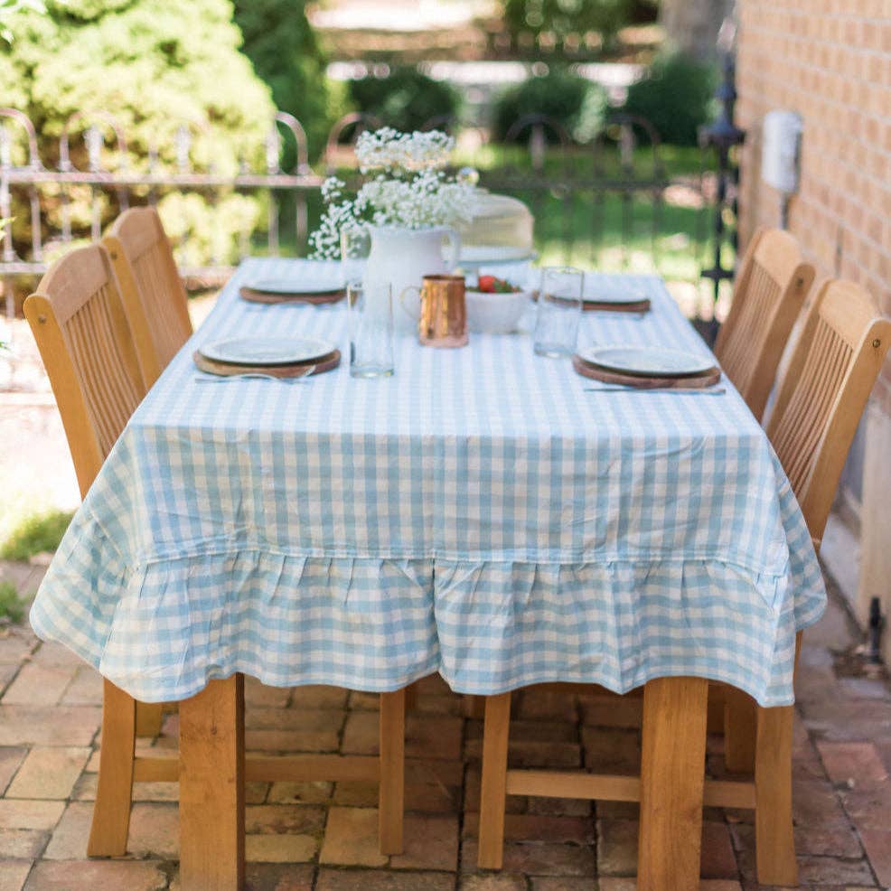 Outdoor dining table set with a blue gingham tablecloth, chairs, and a vase of flowers.