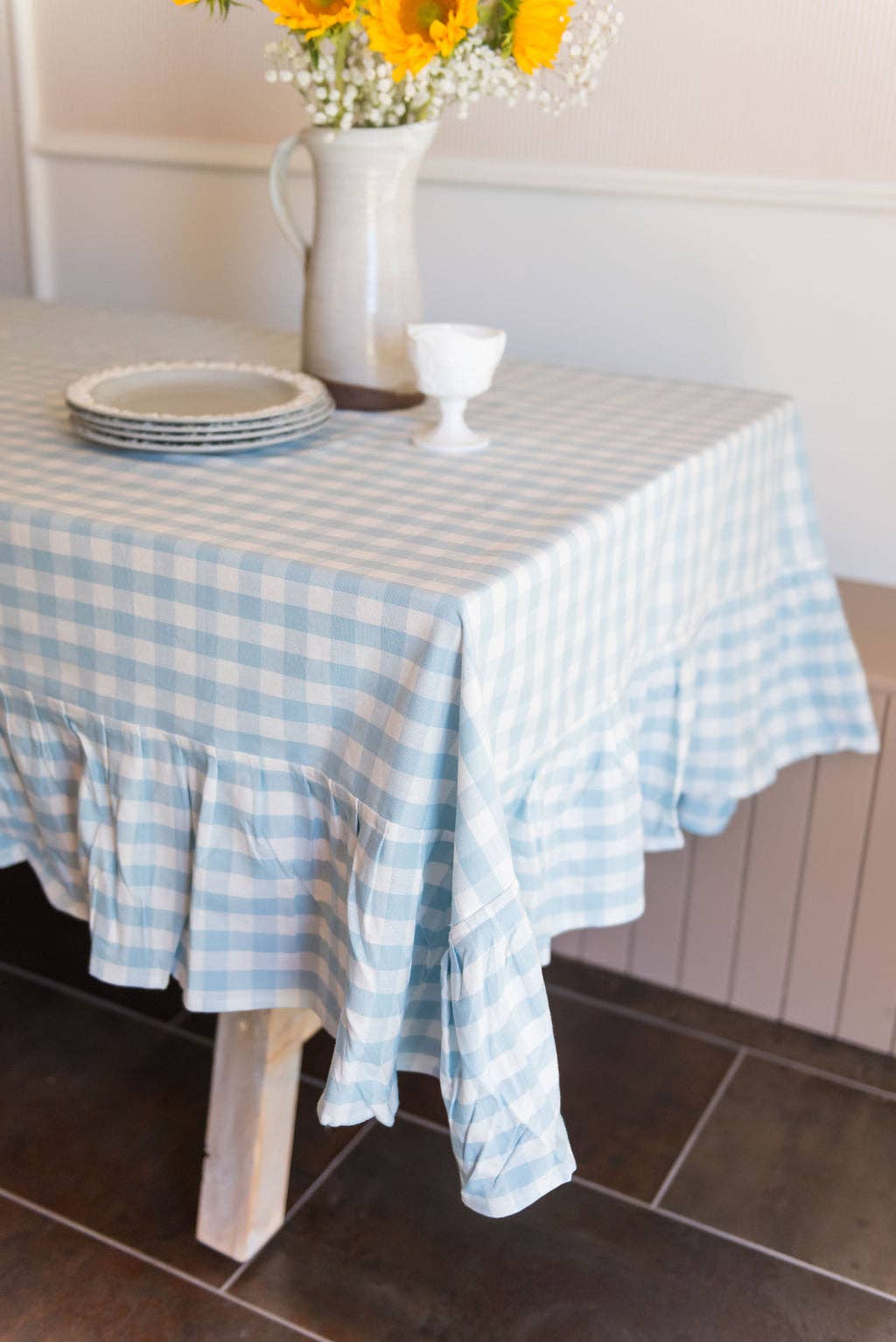 Table with a blue and white gingham tablecloth, plates, and a vase of sunflowers.