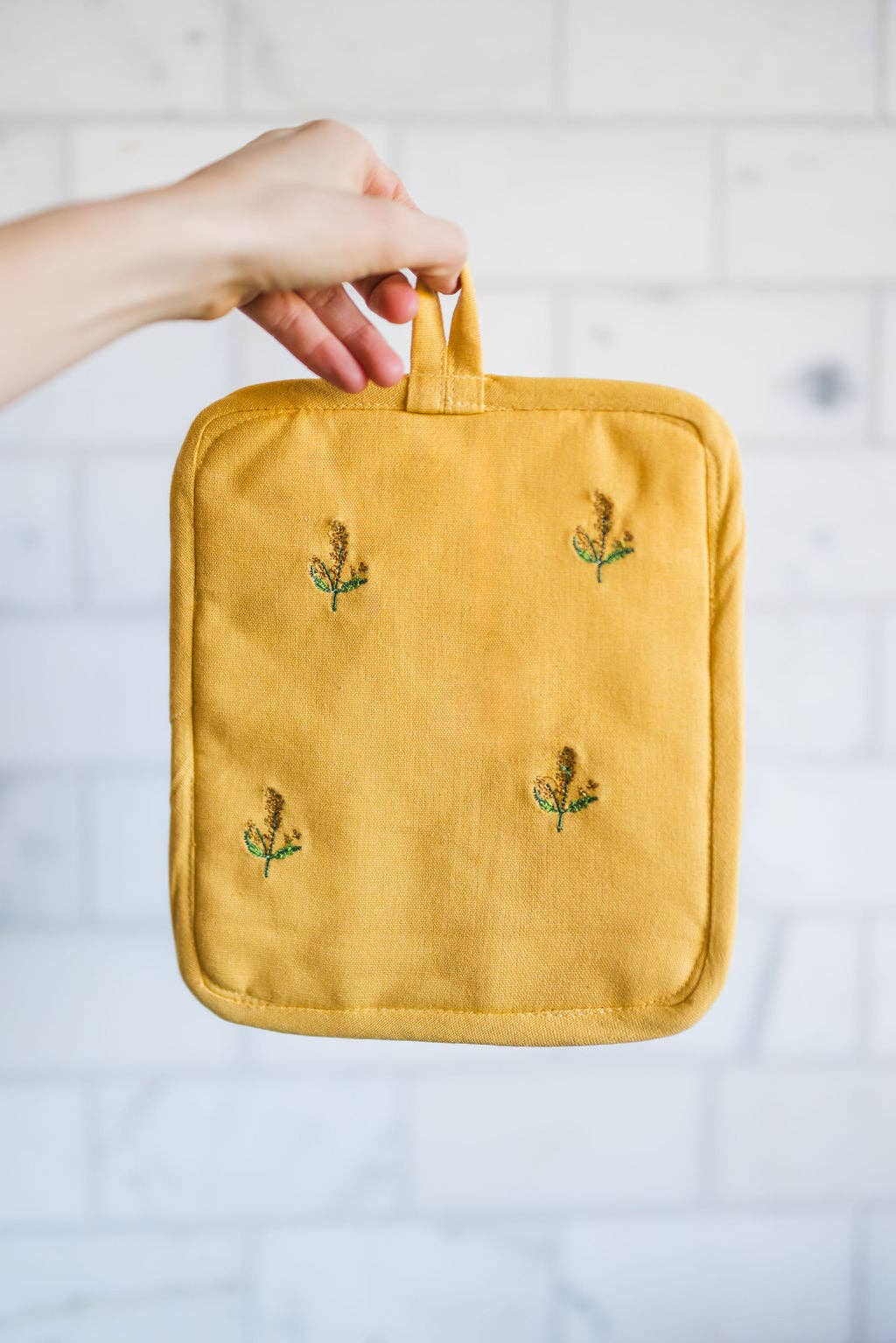Yellow pot holder with floral embroidery held by a hand against a white background