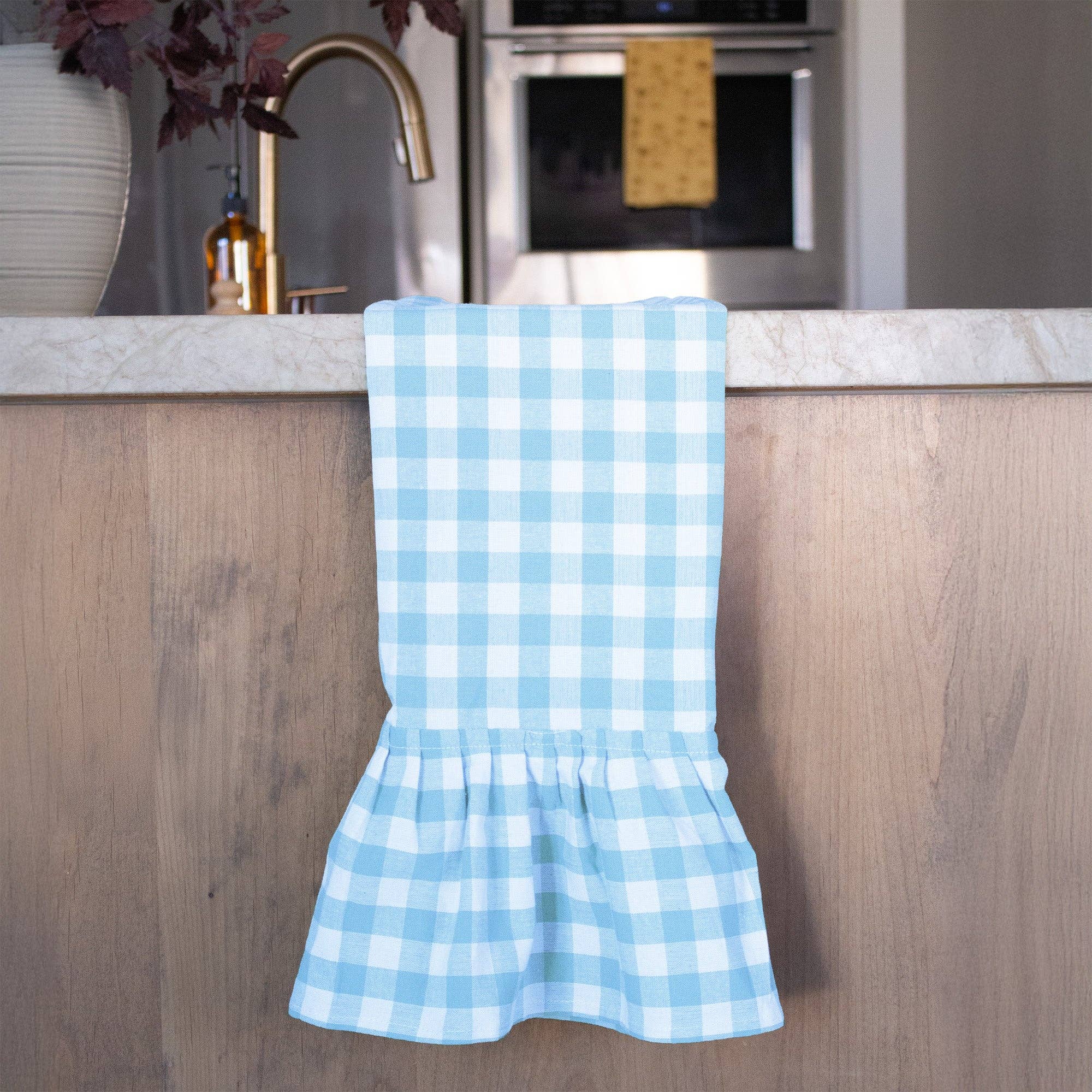 Blue and white gingham checkered dish towel hanging on a wooden kitchen counter.