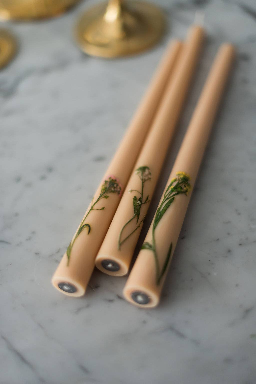Three beige candles with floral designs on a marble surface
