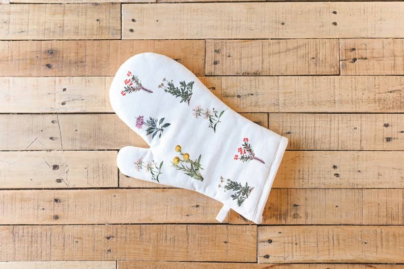 White oven mitt with floral embroidery on a wooden surface
