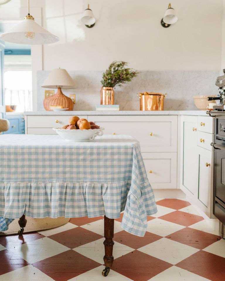 Kitchen with blue gingham ruffle tablecloth, potted plants, and decorative items.