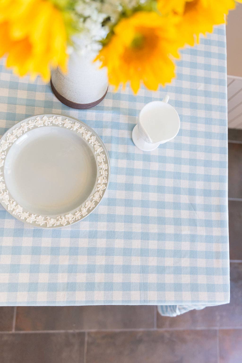Table setting with a blue and white checkered tablecloth, white plates, and yellow flowers.