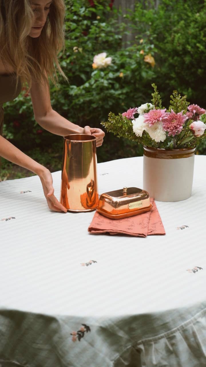 Person interacting with copper vases and a soap dish on a table outdoors.