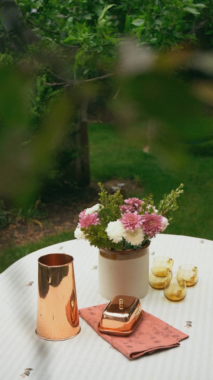 Decorative setting with flowers, candles, and a small statue on a table outdoors.