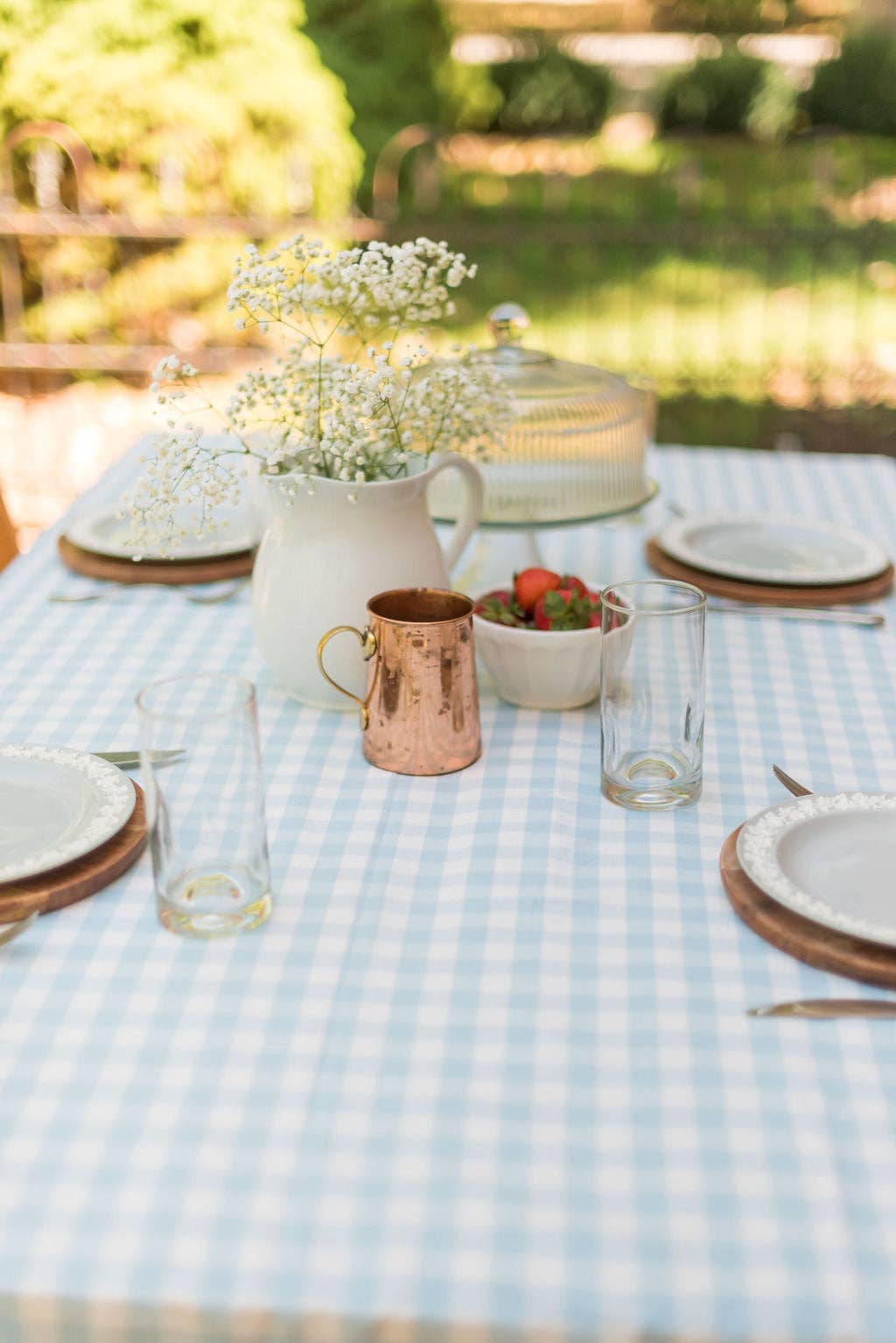Outdoor table setting with a blue checkered tablecloth, flowers, and cutlery.